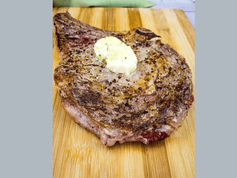 A steak on a cutting board with butter on it.