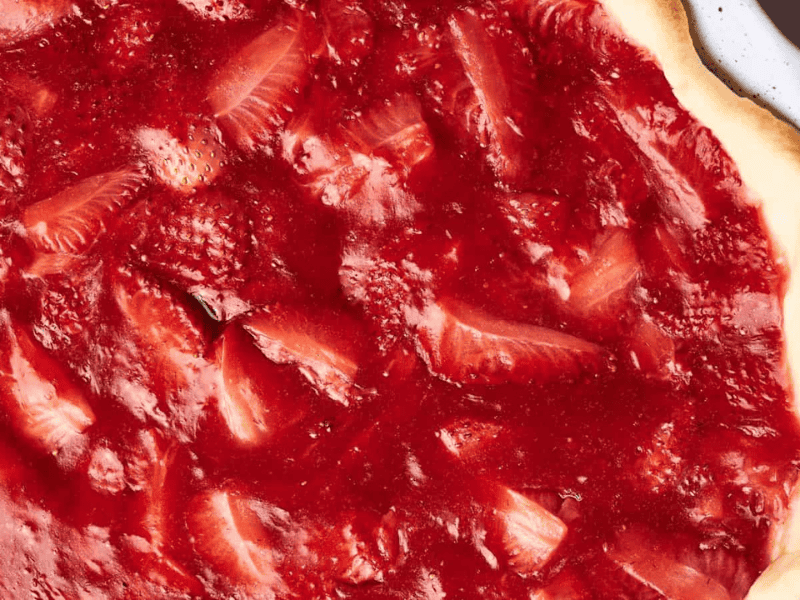 Close-up of a strawberry pizza featuring a thin crust topped with a layer of strawberry sauce and sliced strawberries, evoking the delightful appearance of a strawberry pie with its vibrant red color.
