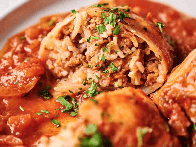 Close-up of stuffed cabbage rolls filled with rice and ground meat, topped with tomato sauce and garnished with chopped herbs.