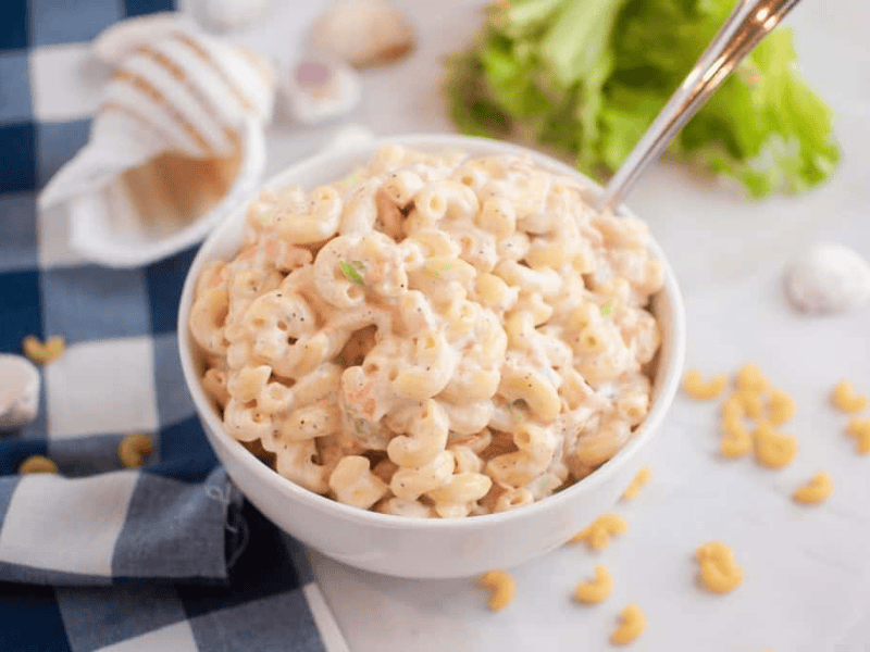 A white bowl filled Hawaiian with macaroni salad with a spoon inside.