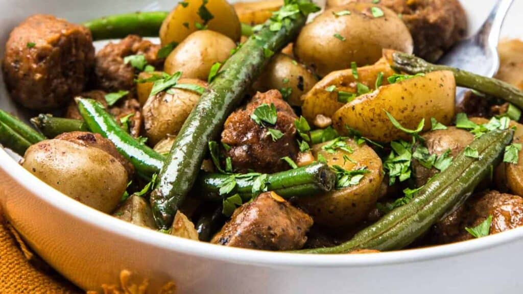 A bowl of cooked potatoes, green beans, and sausage pieces garnished with chopped parsley.