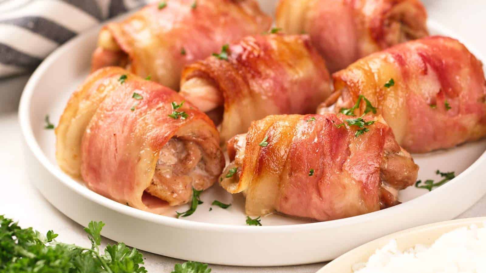 Four bacon-wrapped chicken thighs with parsley garnish on white plate.
