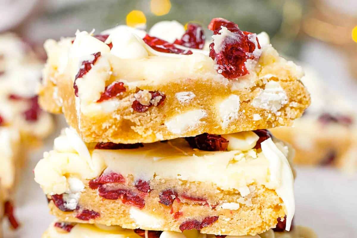 Three stacked bars with a golden base, white chocolate chips, dried cranberries, and a white drizzle on top.