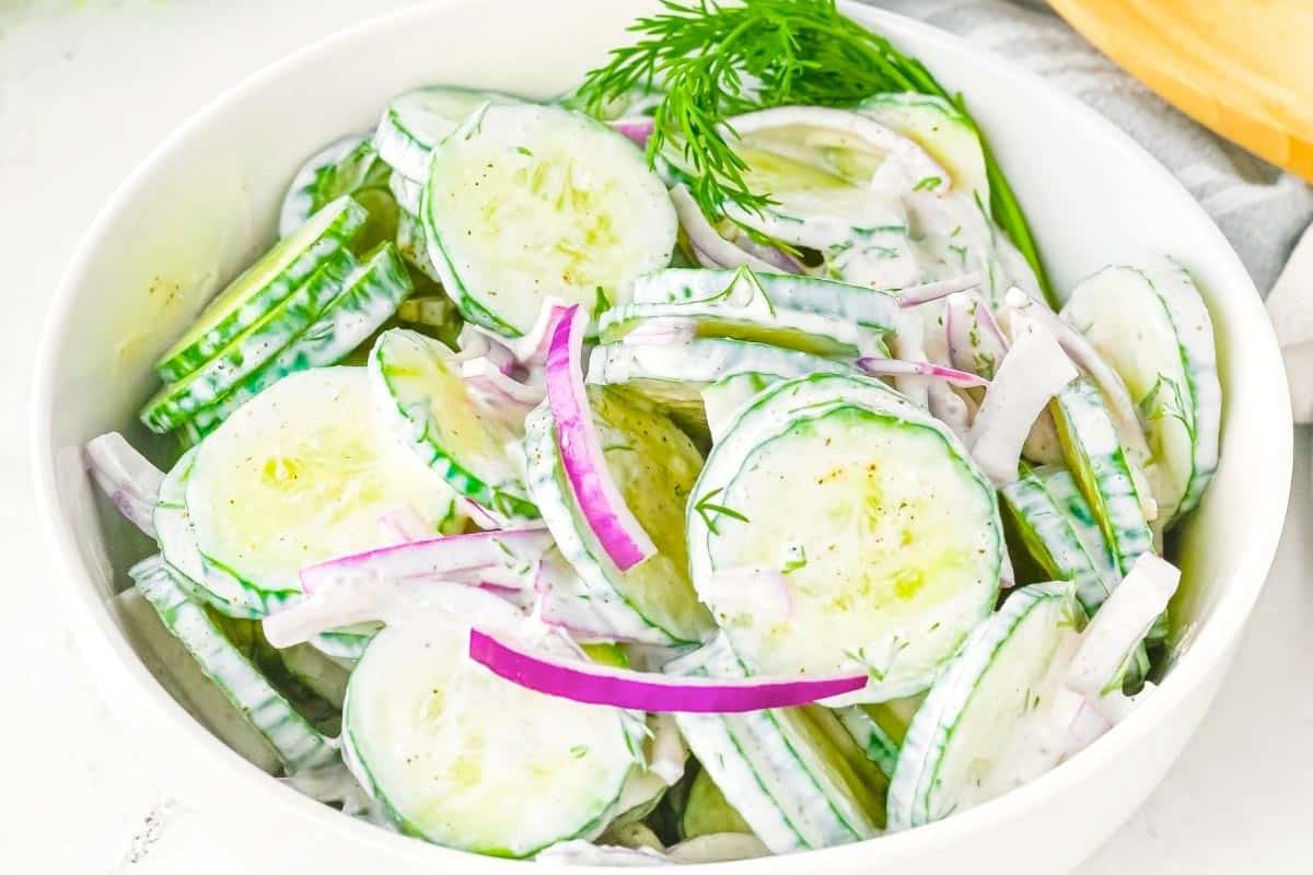 Bowl of cucumber salad with sliced cucumbers, red onions, and creamy dressing, garnished with fresh dill.