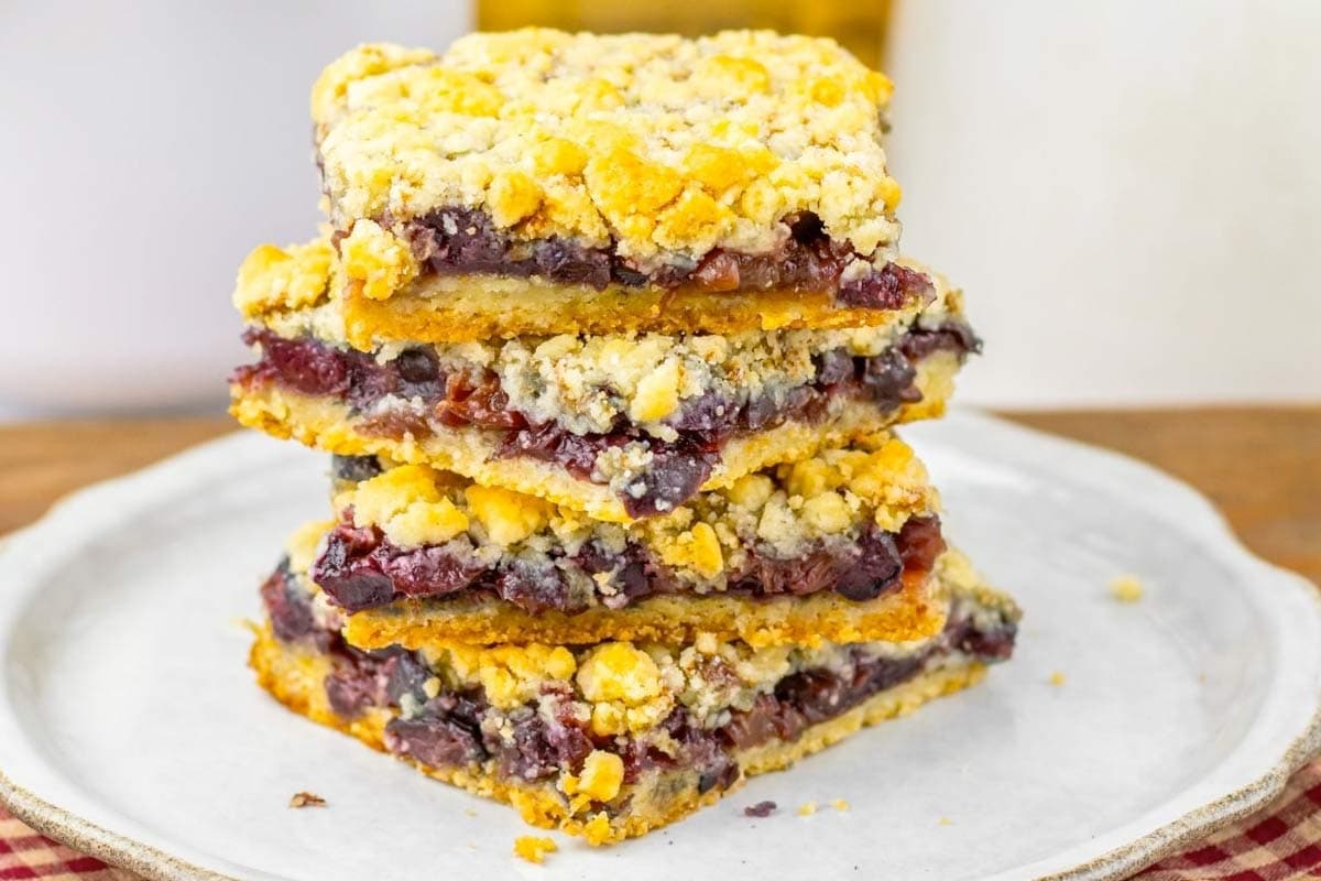 A stack of four fruit crumble bars with a golden crumb topping and visible berry filling, arranged on a white plate.