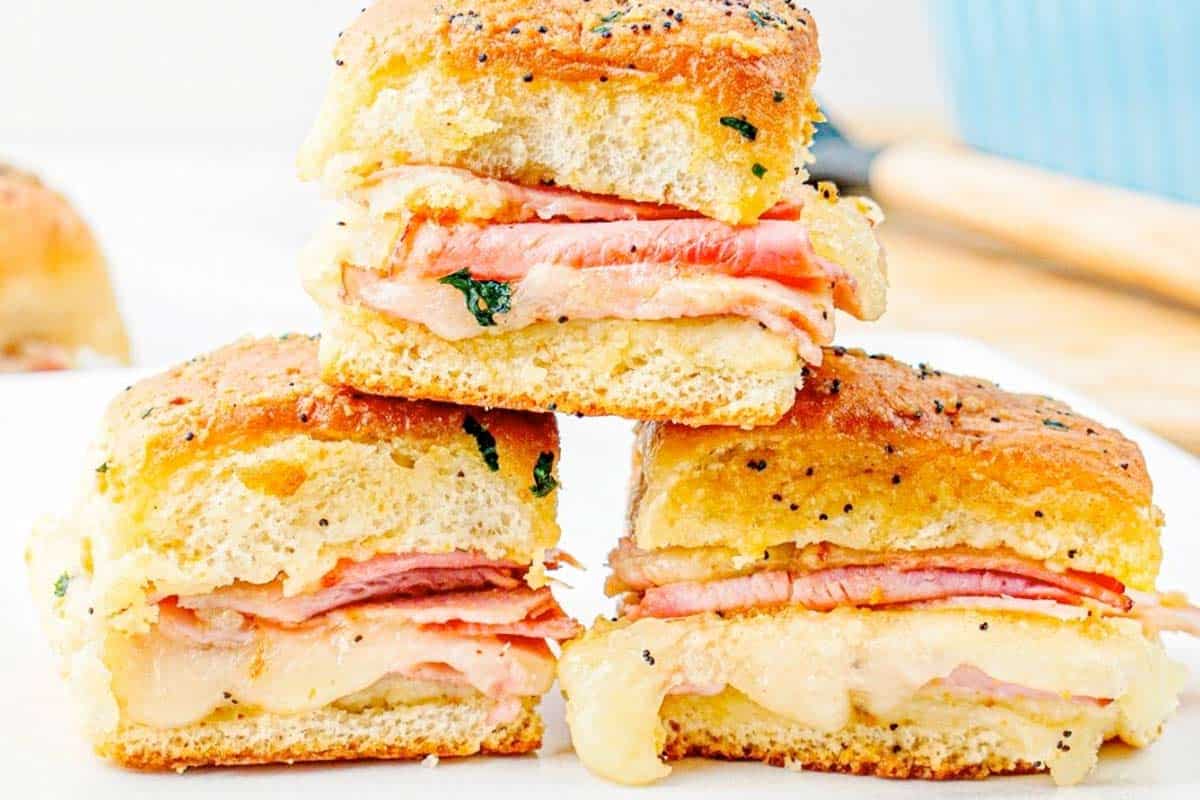 Three ham and cheese sliders stacked on a white plate.