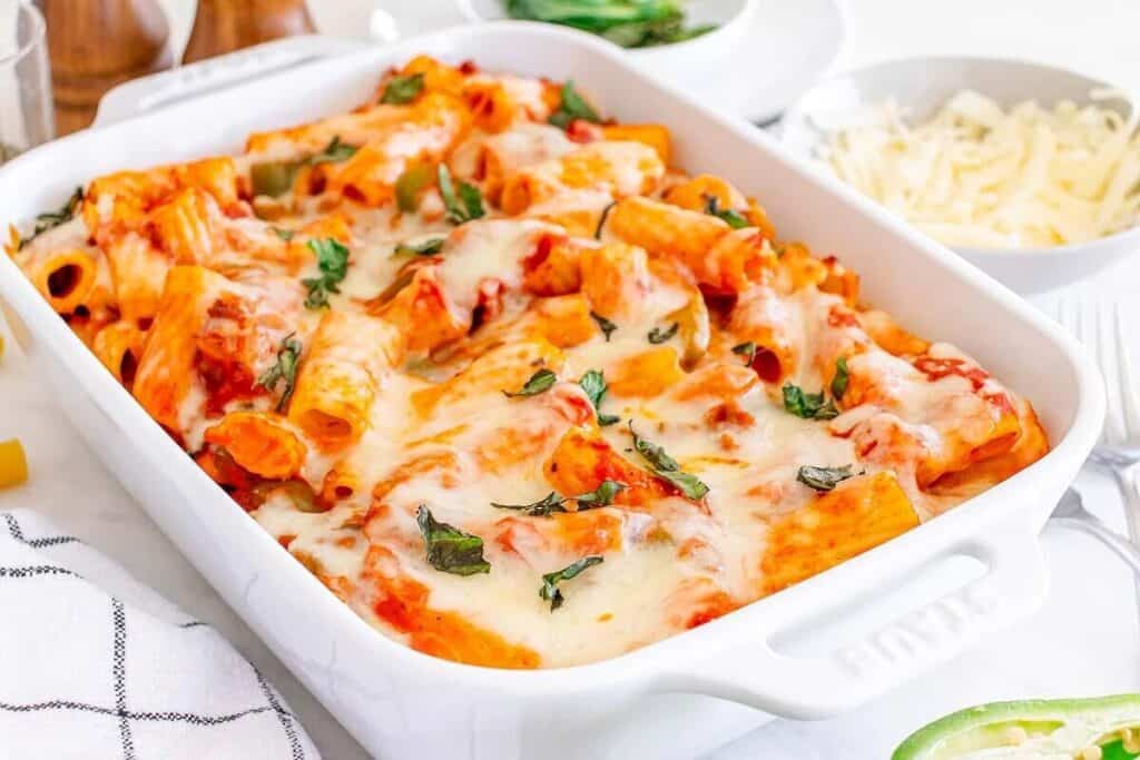Baked pasta with melted cheese and tomato sauce, garnished with fresh basil, served in a white rectangular dish.