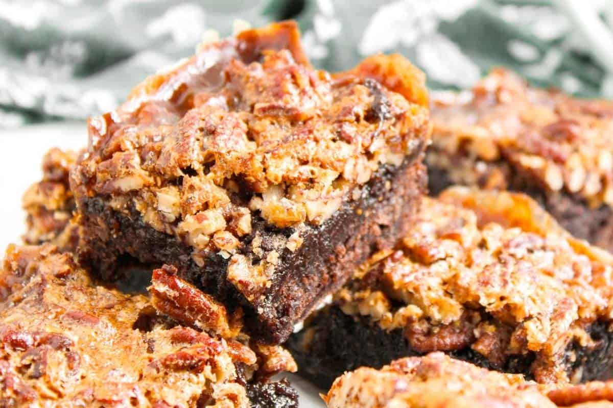 Close-up of pecan pie bars with a layer of pecans and caramelized topping over a dense, dark brownie base.