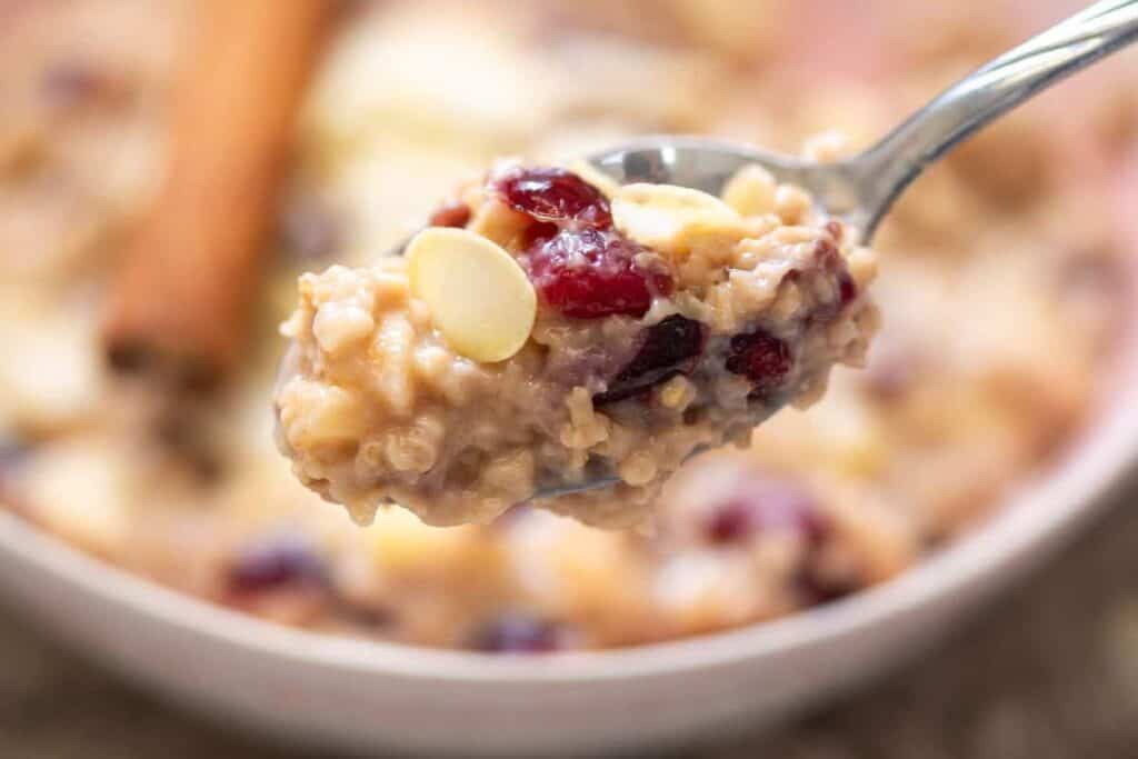 A close-up of a spoonful of oatmeal with dried cranberries and white chocolate chips, held above a bowl of the same mixture.