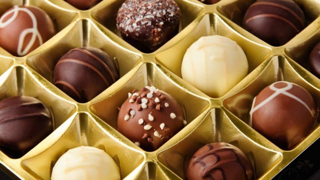 A close-up of assorted chocolate truffles in a gold plastic tray, featuring various flavors and decorative toppings.