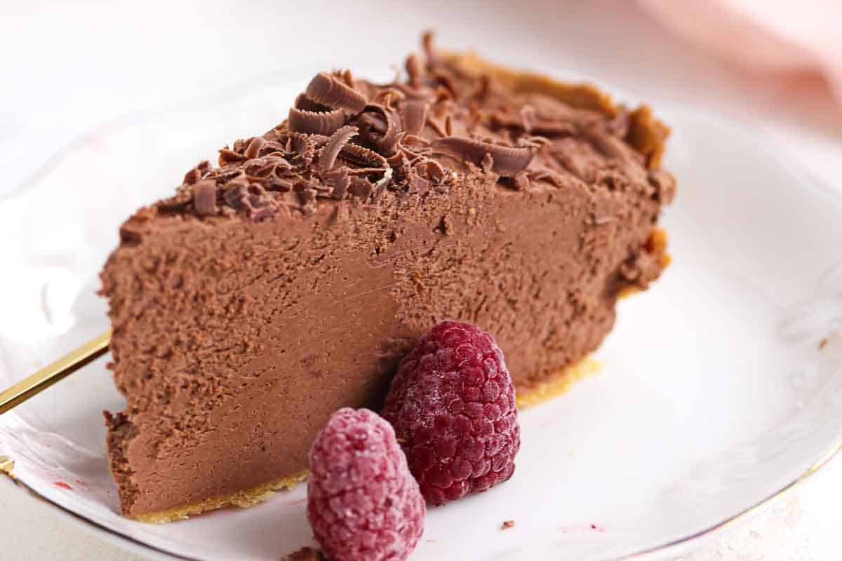 A slice of chocolate mousse pie on a white plate, topped with chocolate shavings and served with two raspberries.