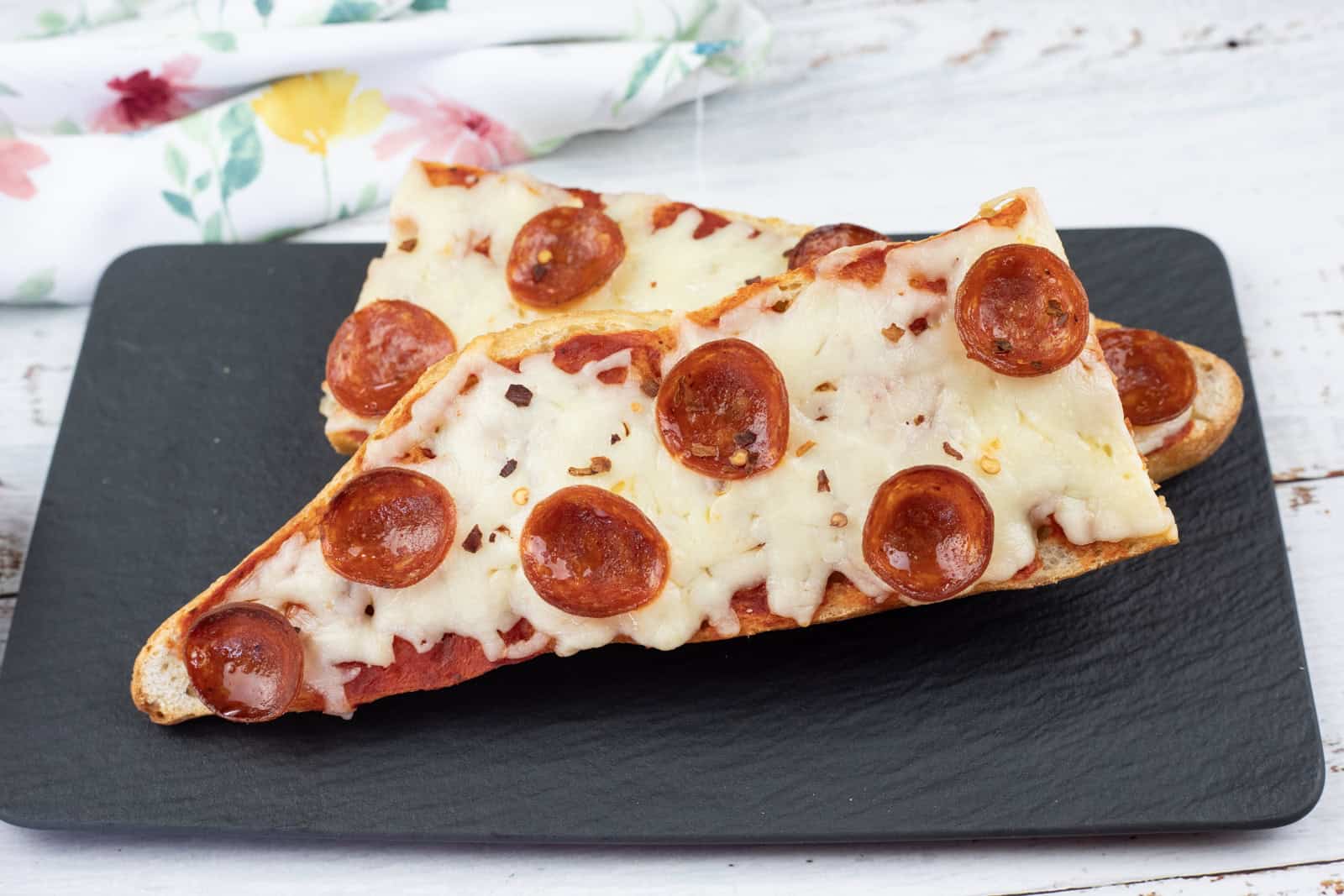 Two slices of French bread pizza topped with melted cheese and pepperoni are placed on a black rectangular plate.