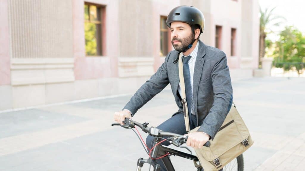 A man in a suit and helmet rides a bicycle outdoors, carrying a messenger bag.
