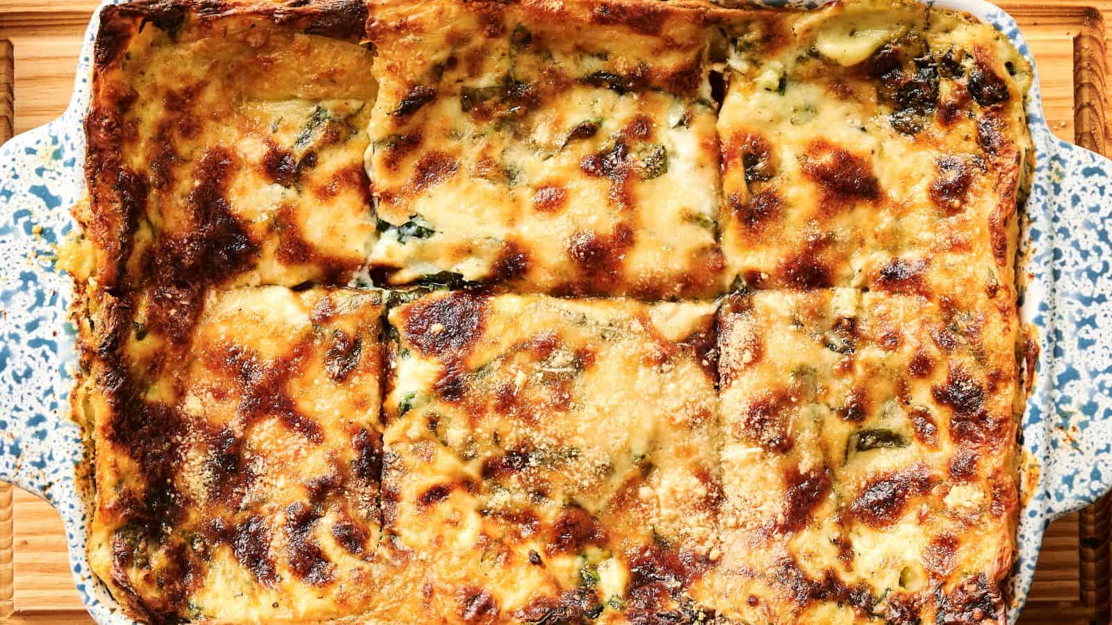 Baked lasagna in a rectangular dish, sliced into six pieces with a golden, browned cheese topping.