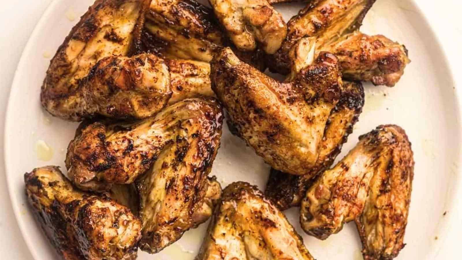 A plate of seasoned, grilled chicken wings arranged on a white surface.