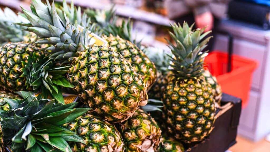 A pile of fresh pineapples with green leaves, displayed for sale in a store.