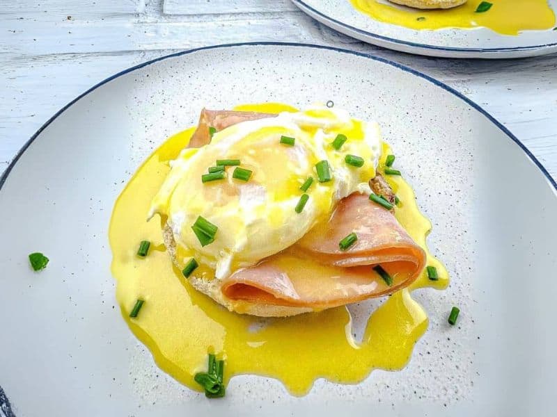 Eggs Benedict with poached eggs, ham, and hollandaise sauce on a plate, garnished with chives.