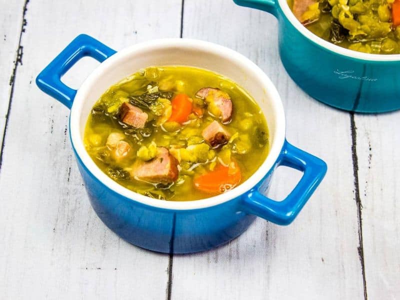 Two bowls of soup with ham, sausage, split peas and vegetables in them.