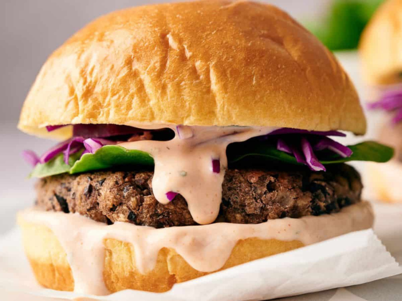 A black bean burger in a burger bap with relish oozing out over it.