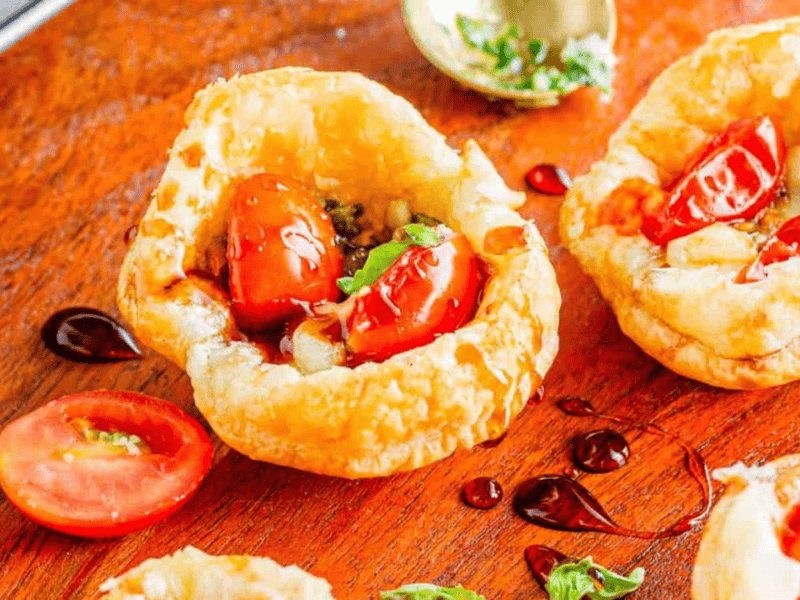 Fresh cherry tomatoes and herbs served in crispy puff pastry cups on a wooden surface.