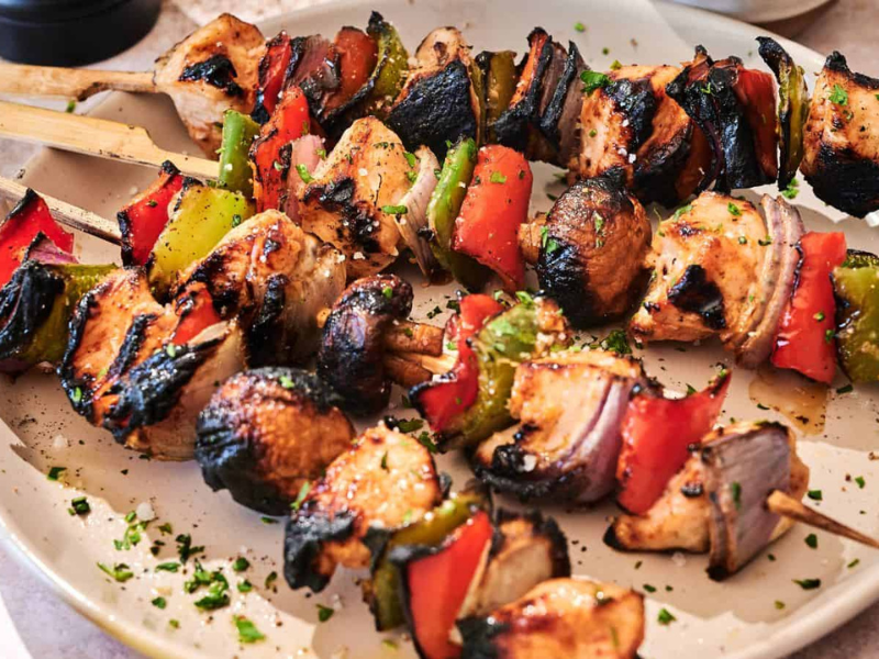 Grilled chicken skewers with red bell peppers, green bell peppers, and onions are served on a white plate, garnished with chopped herbs.