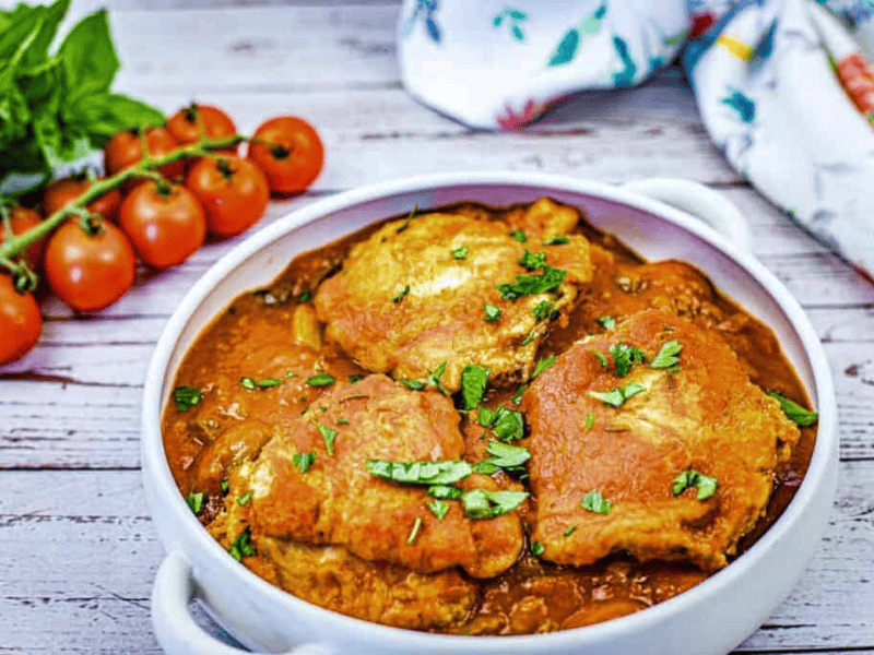 A white dish filled with pieces of Chicken Cacciatore in a red sauce, garnished with chopped herbs.