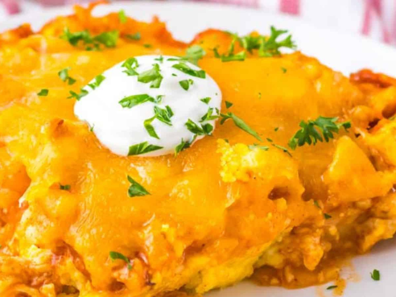 A serving of chicken tamale pie topped with a dollop of sour cream and garnished with chopped herbs on a white plate.