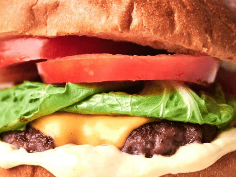 Close-up of a copycat smash burger with lettuce, tomato, and a thick beef patty on a sesame seed bun.