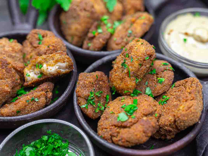 Three bowls filled with golden-brown chicken nuggets garnished with chopped parsley, served with a small bowl of creamy dipping sauce.