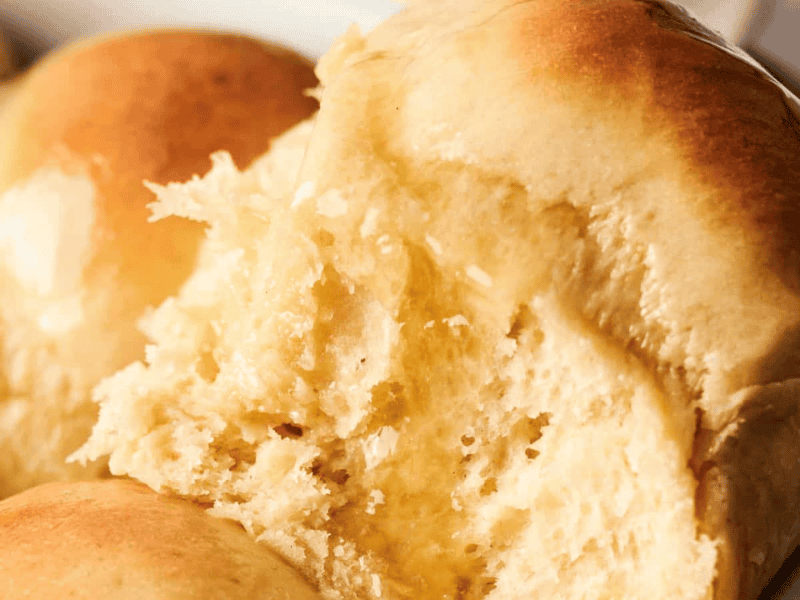 Close-up of freshly baked golden-brown dinner rolls, with one roll partially torn to show its soft, fluffy interior.