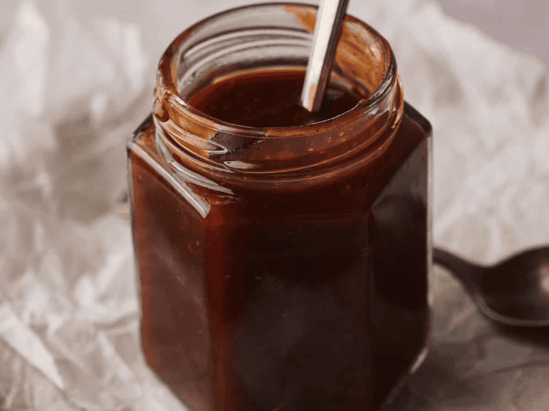 Homemade BBQ sauce in a jar with two spoons by the side.