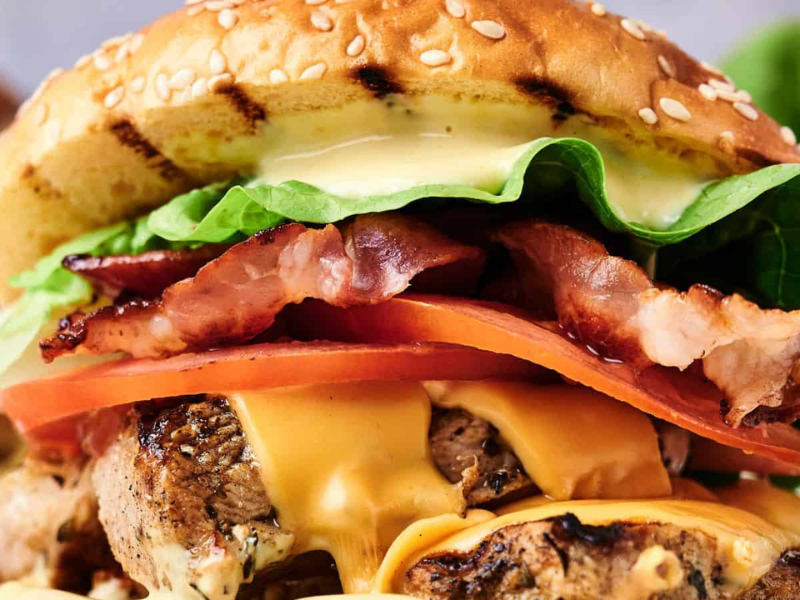 Close-up of a cheeseburger with a sesame bun, bacon, lettuce, tomato, cheese, and beef patty.