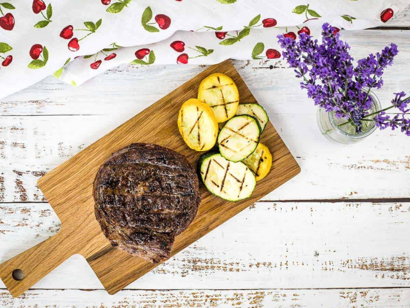 A top-down shot of Grilled Ribeye Cap Steak on a cutting board with veggies.