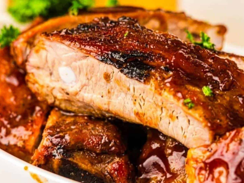 Close-up of Grilled ribs covered in sauce, garnished with chopped parsley, served on a white plate.