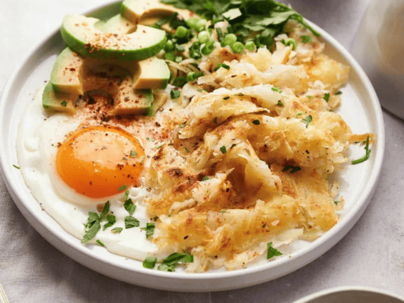 Hash Browns on a white plate with an egg and avocado.