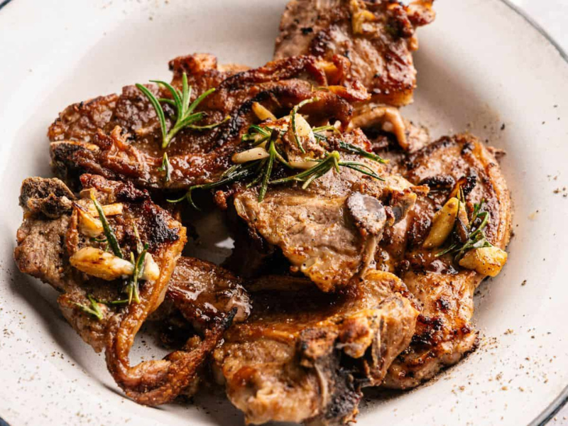 Grilled lamb chops garnished with rosemary and garlic, served on a white plate.