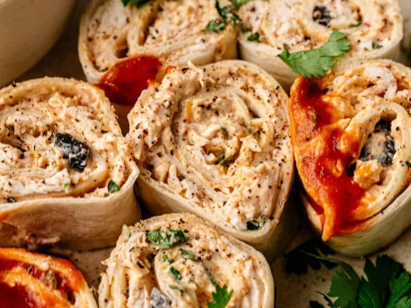 Close-up of several tortilla pinwheel roll-ups filled with shredded chicken, herbs, and sauce, garnished with cilantro.