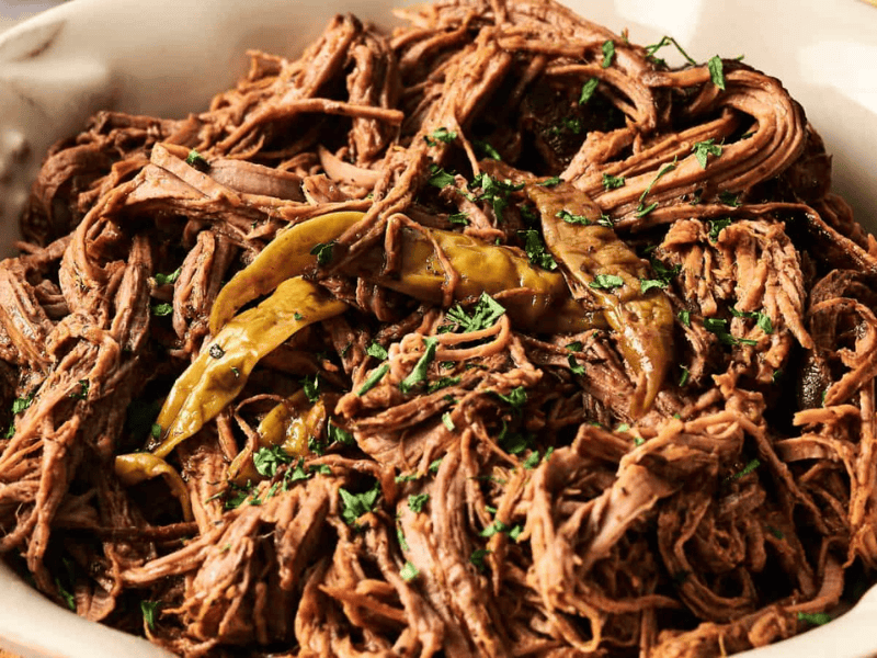 A bowl of shredded beef garnished with cilantro and peppers.