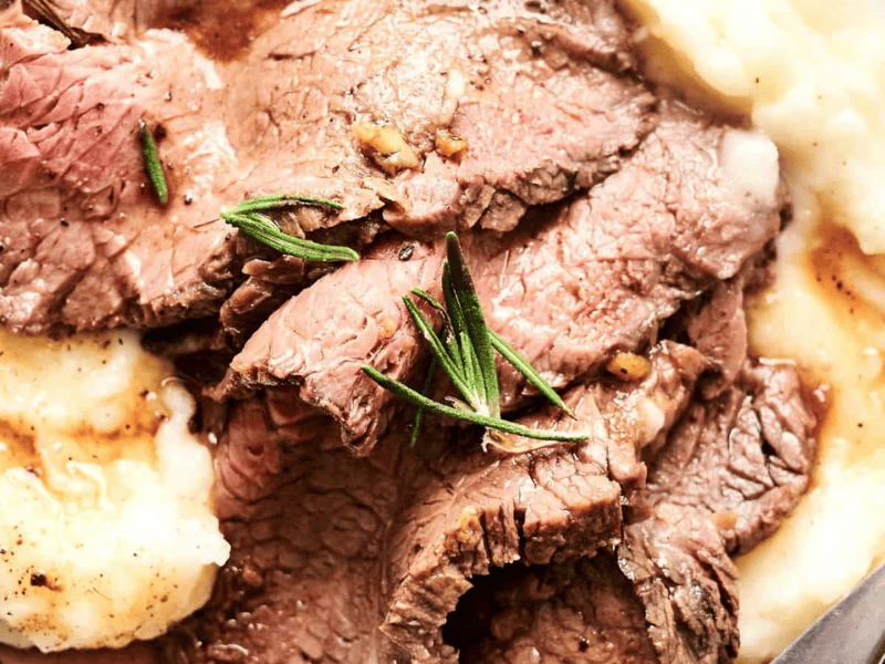 Sliced roast beef served on a bed of mashed potatoes, garnished with fresh rosemary.