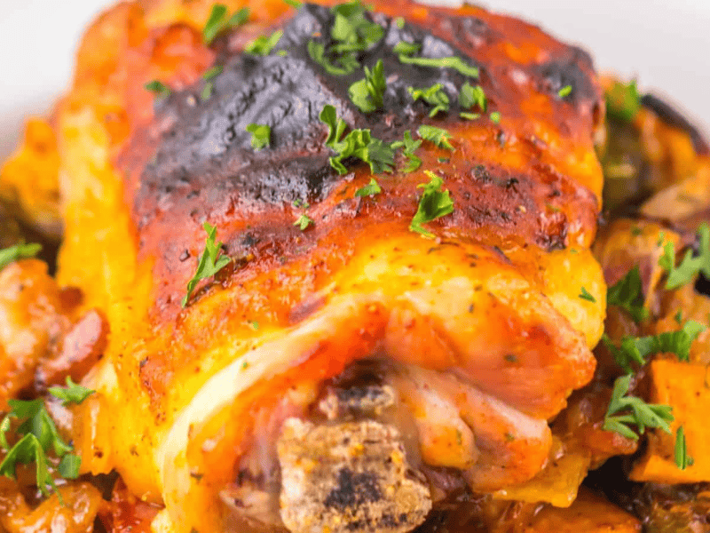 Roasted chicken thigh with herbs, served on a bed of roasted vegetables.