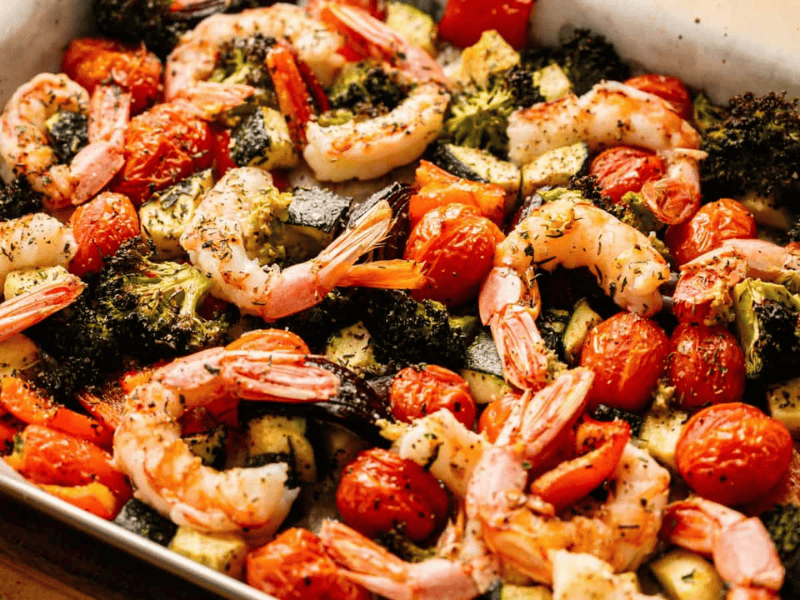 Sheet pan of roasted shrimp, cherry tomatoes, broccoli, and zucchini, seasoned with herbs and baked on parchment paper.