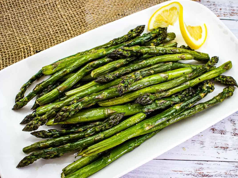Smoked asparagus on a white platter with lemon.