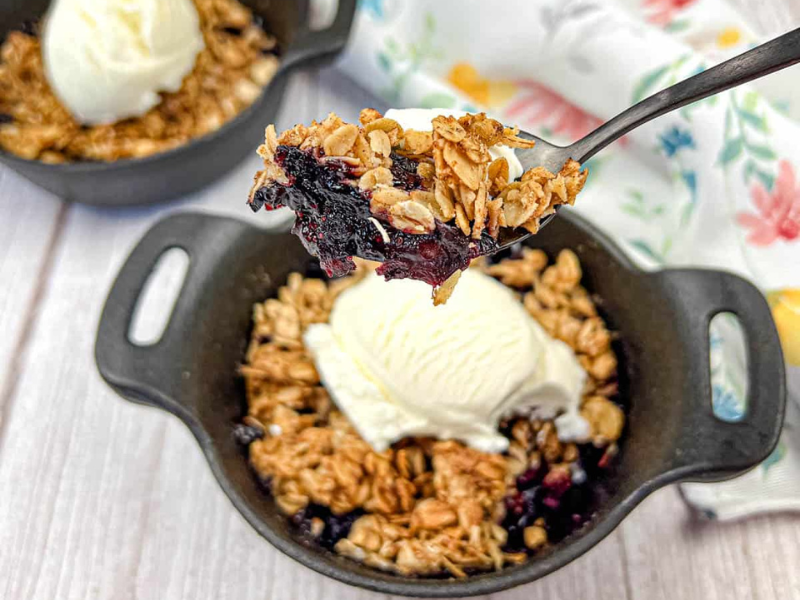 A spoon lifts a portion of Smoked Berry Crisp from a bowl.
