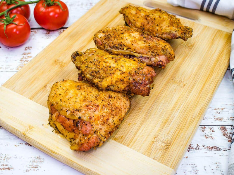Chicken thighs on a cutting board with tomatoes.
