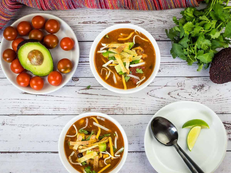 Smoked Chicken Tortilla Soup in two white bowls with garnishes nearby.