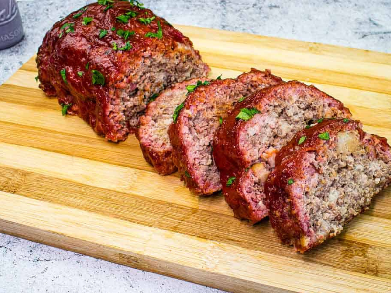 Sliced Smoked Meatloaf on a cutting board with salt and pepper shakers on the side.
