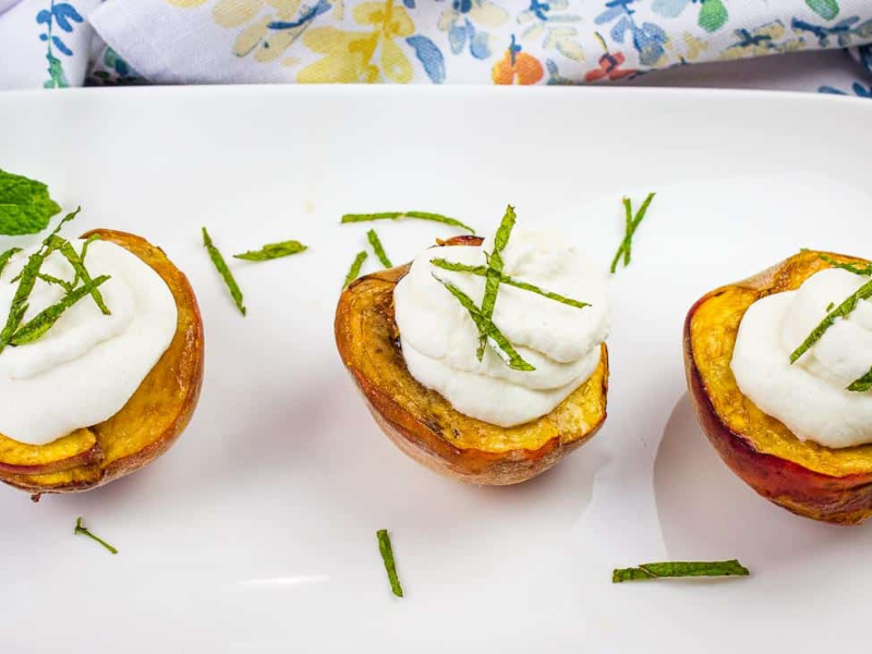 Smoked peaches topped with spiced rum whipped cream on a platter.