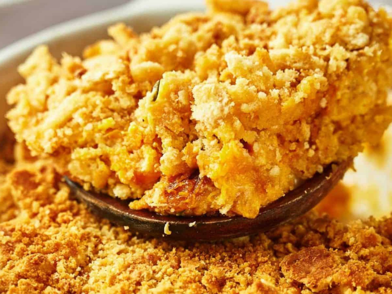 Squash casserole being served with a wooden serving spoon.