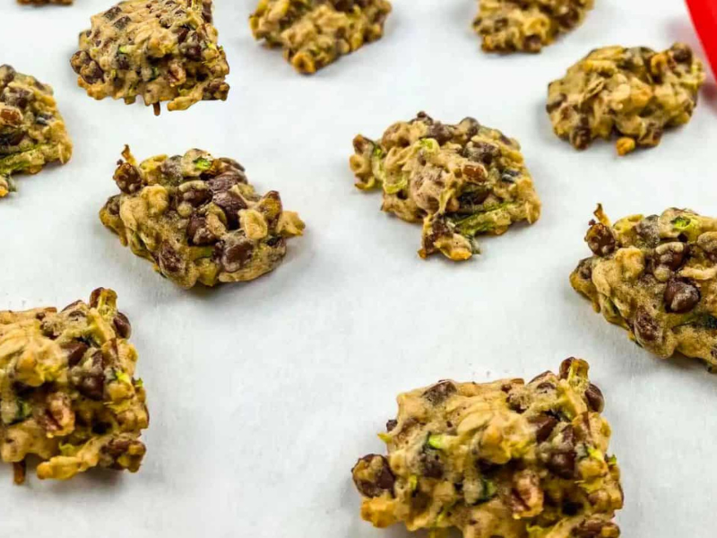 A batch of Zucchini cookies with chocolate & pecan on a parchment-lined baking sheet.
