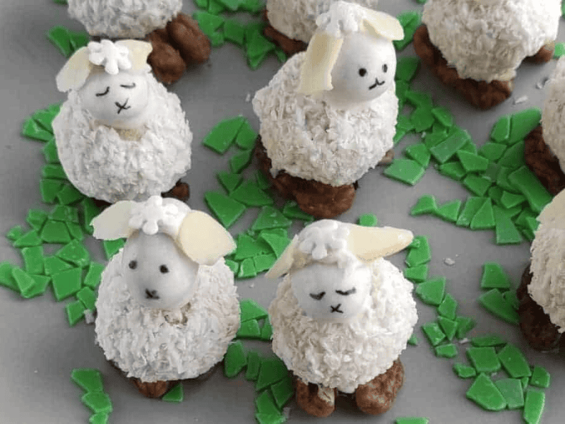 Coconut Easter Bunny Candies with coconut-covered bodies and walnut feet, surrounded by green candy shards on a gray plate.